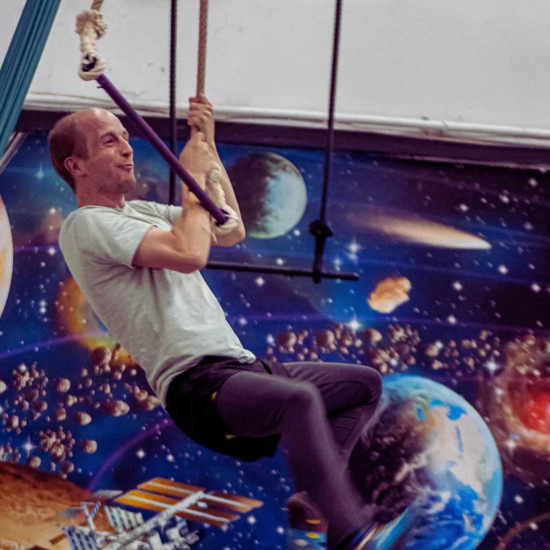 An adult CircusMASH participant practising on a trapeze