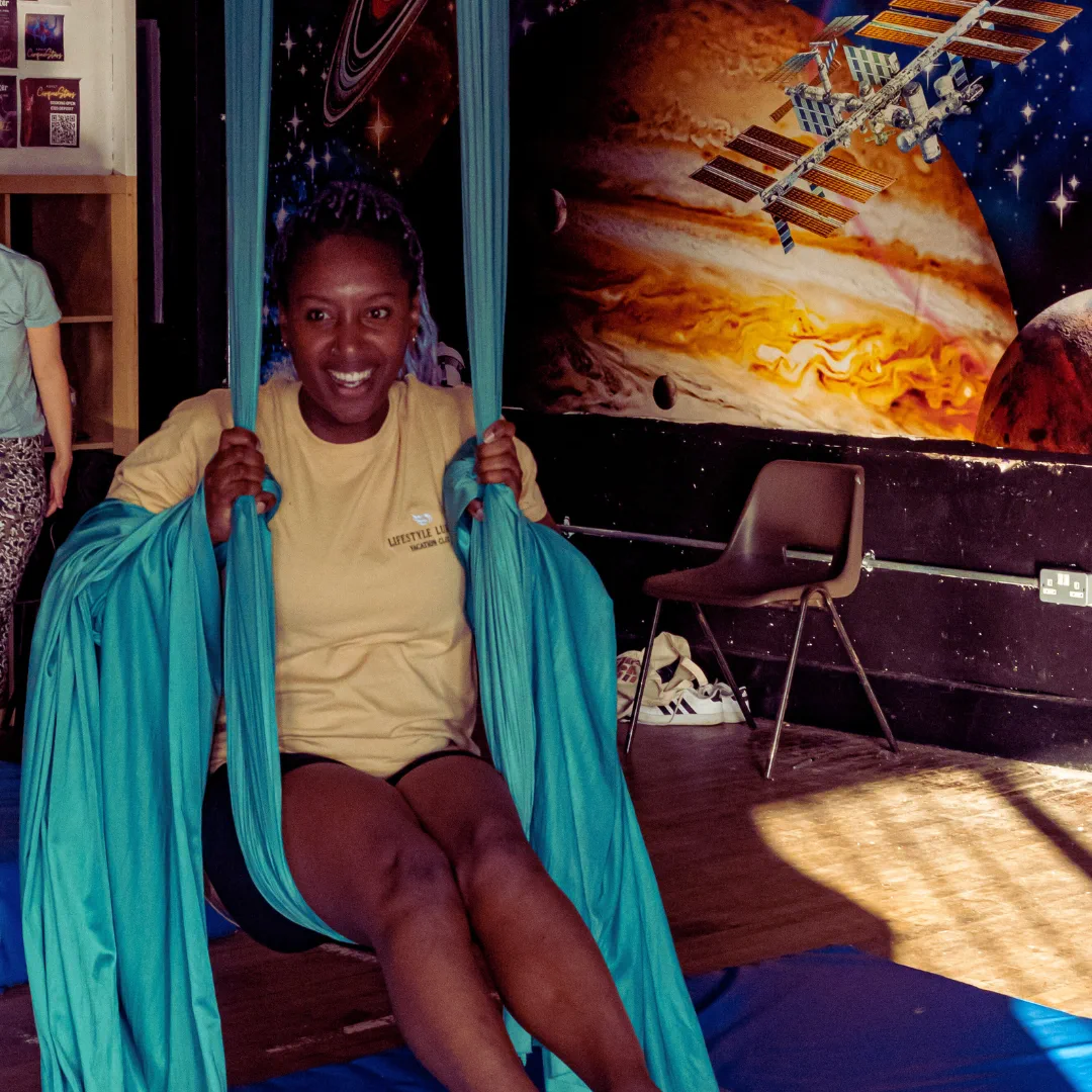 An adult CircusMASH participant smiling while seated in blue aerial silks