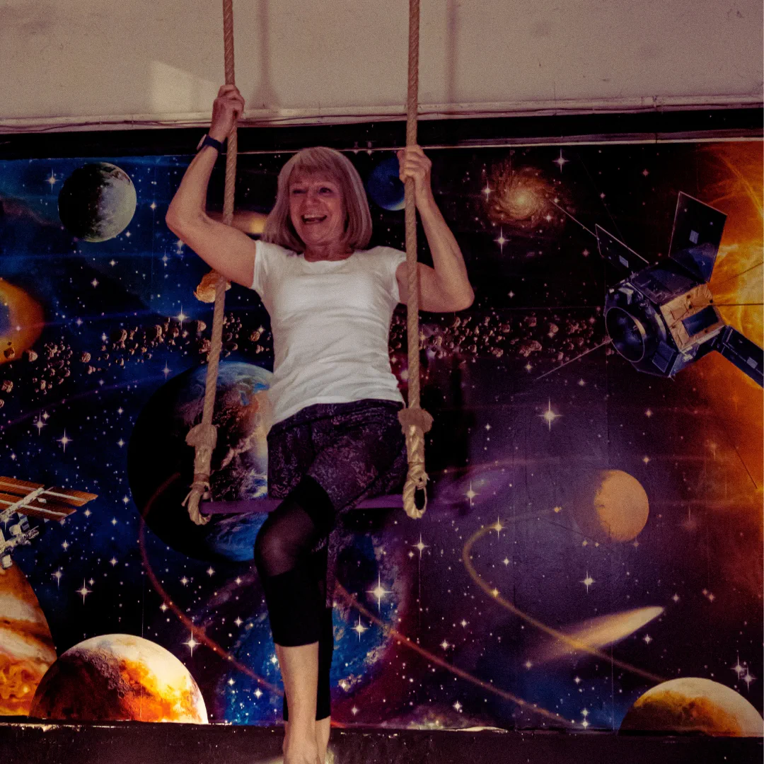 An adult CircusMASH participant smiling on a flying trapeze