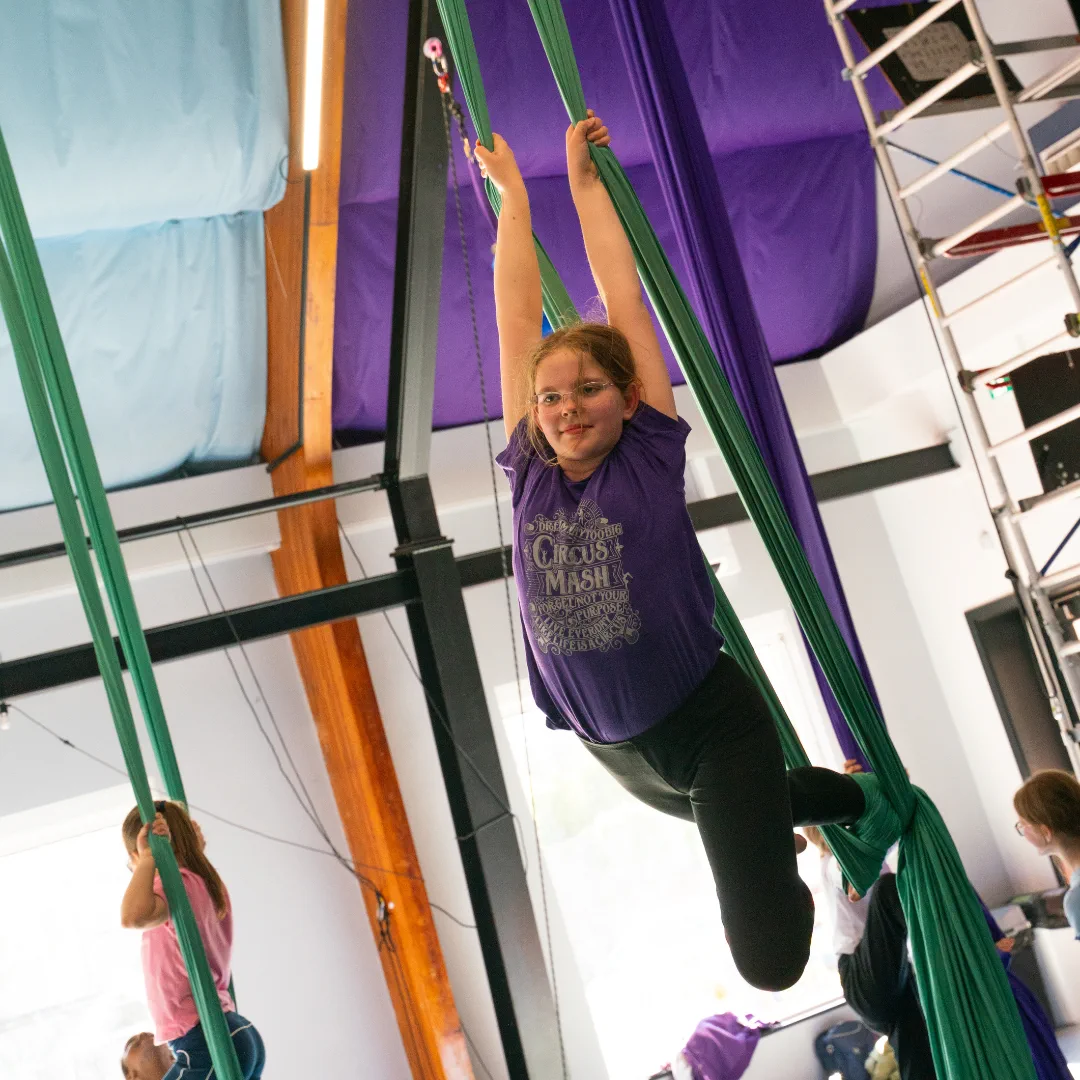 A young CircusMASH participant practising on green aerial silks