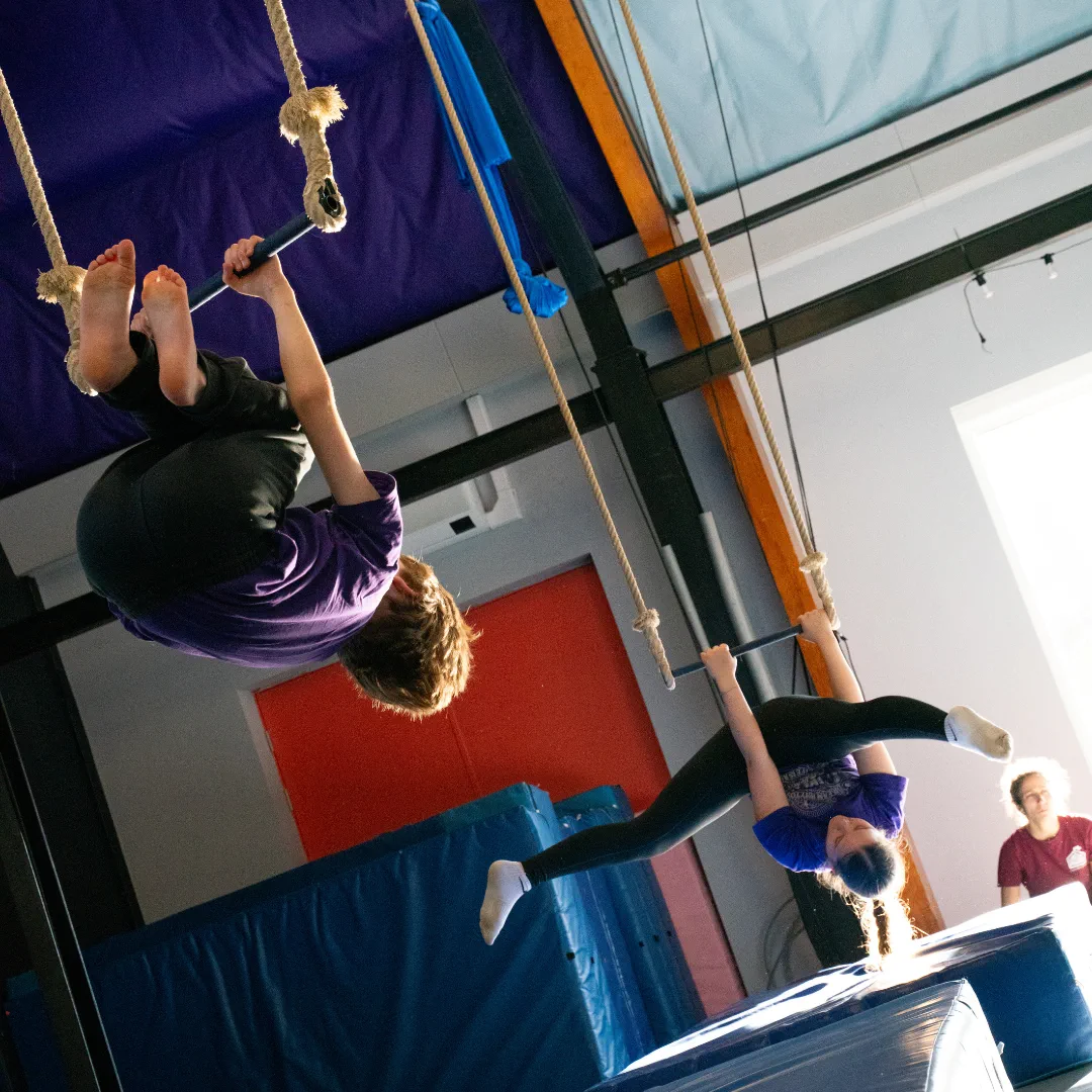 Two young CircusMASH participants practising trapeze skills above crash mats