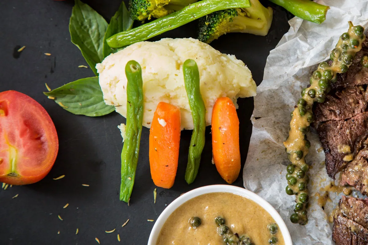 Sliced steak served with vegetables and peppercorn sauce